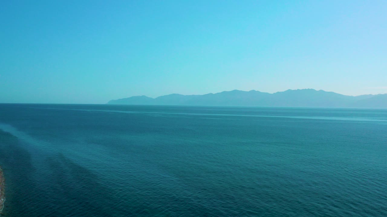 Wide blue sea with distant mountains under clear sky