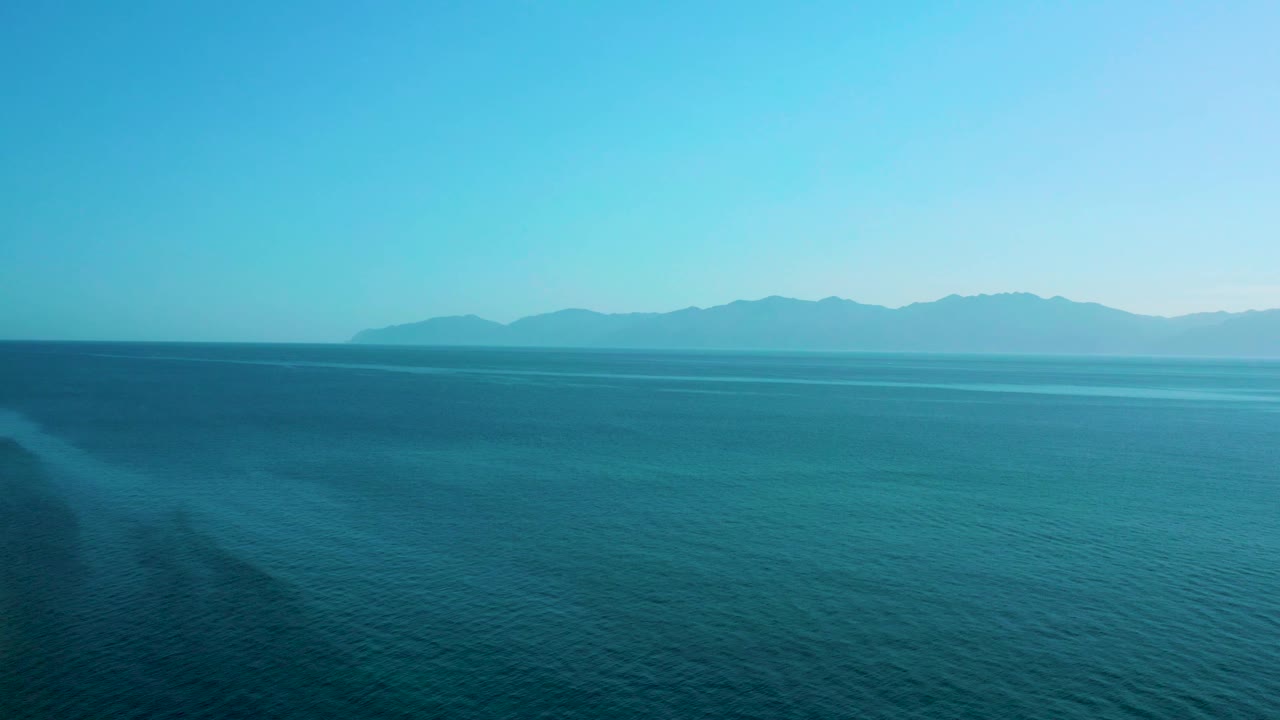 Open sea stretches toward distant mountains in Mexico, with subtle surface ripples and no visible people or vessels.