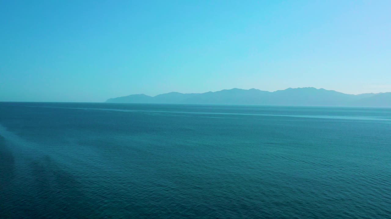 A calm blue water view shows a hazy shoreline and mountain shapes across the horizon near El Sargento La Ventana, with no visible people.