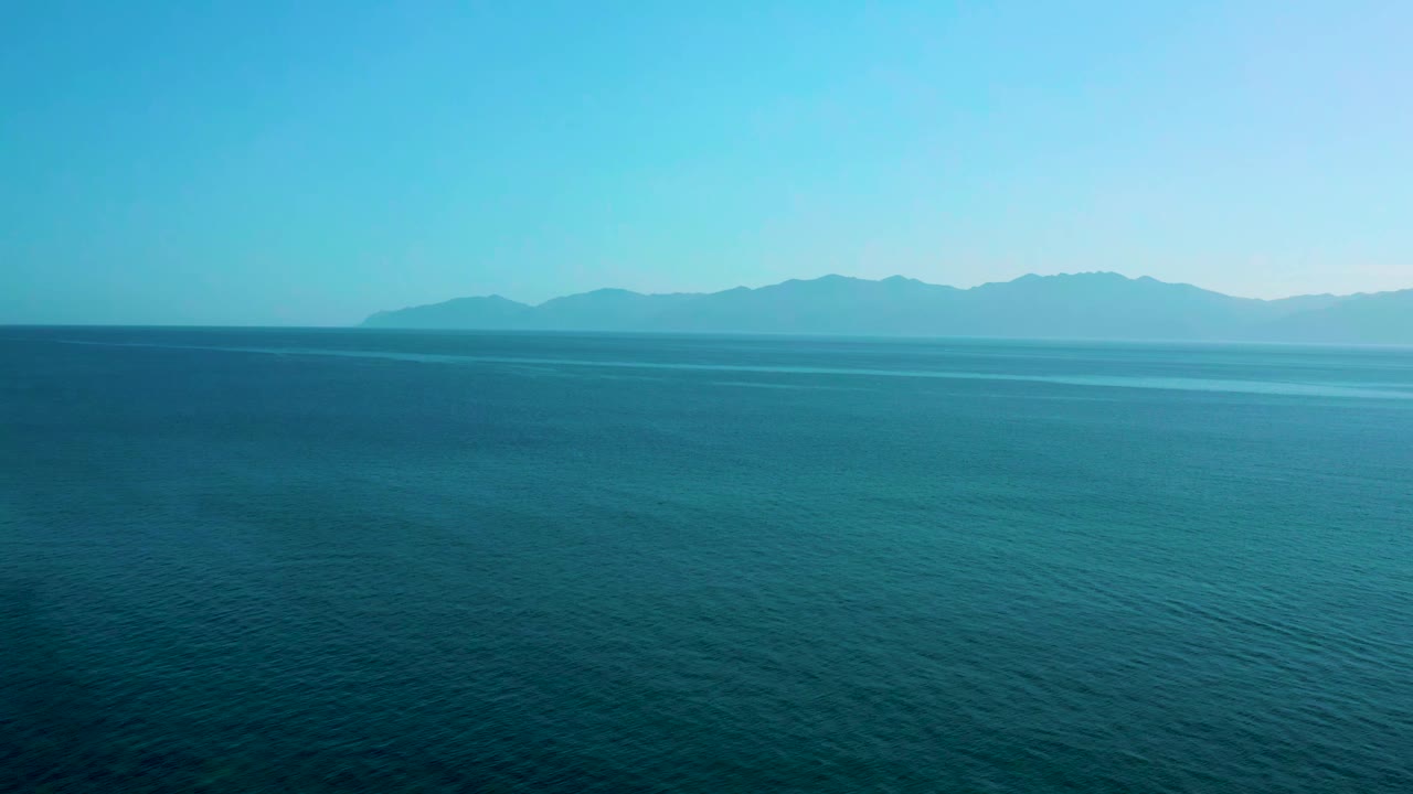High aerial ocean view in El Sargento La Ventana, Mexico, with darker foreground water and a pale mountain ridge beyond the horizon, no visible people.