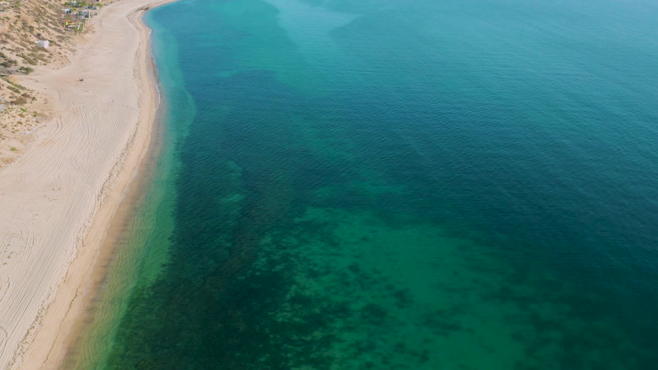 Aerial view over El Sargento La Ventana, Mexico, with the shoreline curving down the left side and broad blue-green water filling most of the frame, with no visible people.