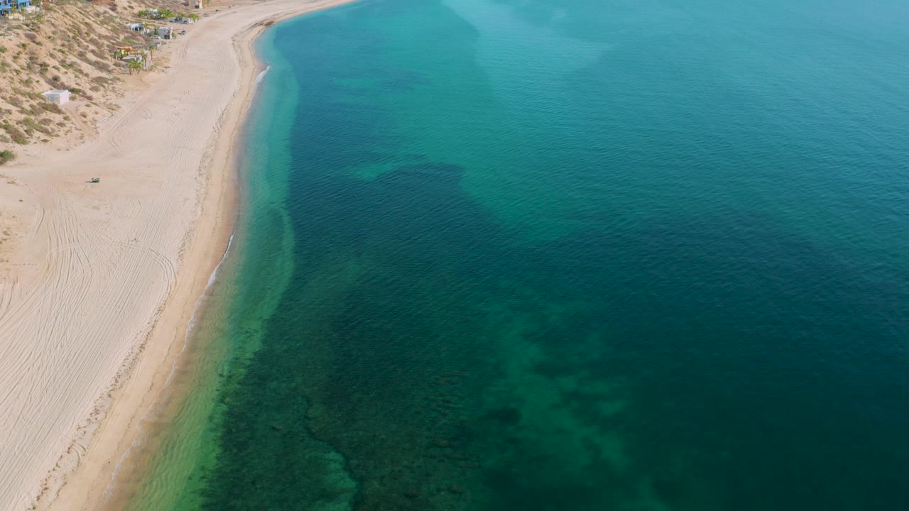 Beach and clear sea with darker seabed areas near shore.