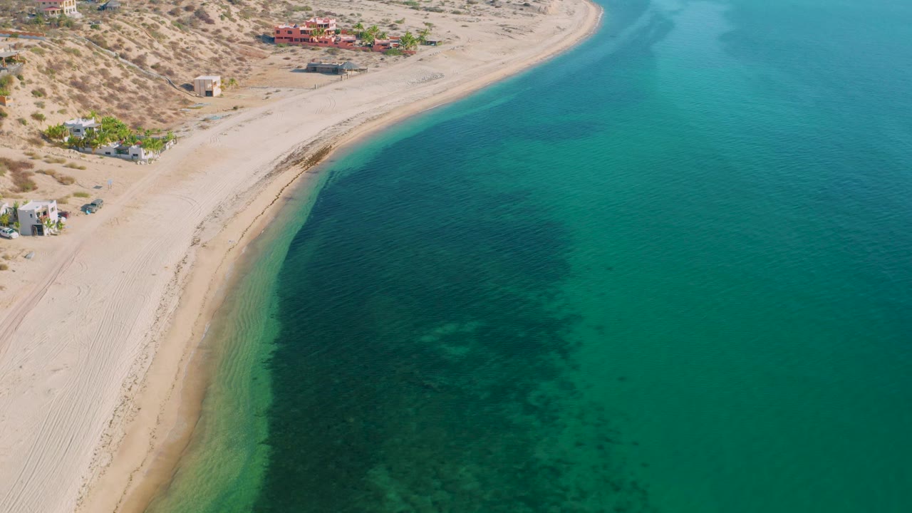 Aerial view of beach, desert vegetation, buildings, and clear coastal water.