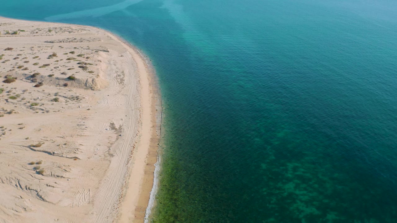 High aerial view in El Sargento La Ventana, Mexico, with a sandy point entering from the left and a broad field of teal water filling the right side, no visible people.