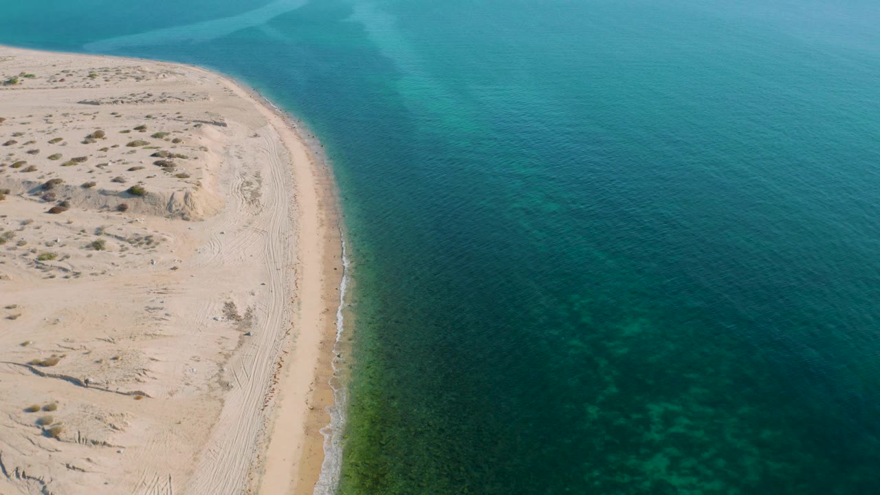 Aerial frame from El Sargento La Ventana, Mexico, where the pale beach is cropped along the left and calm teal sea occupies most of the image, no visible people.