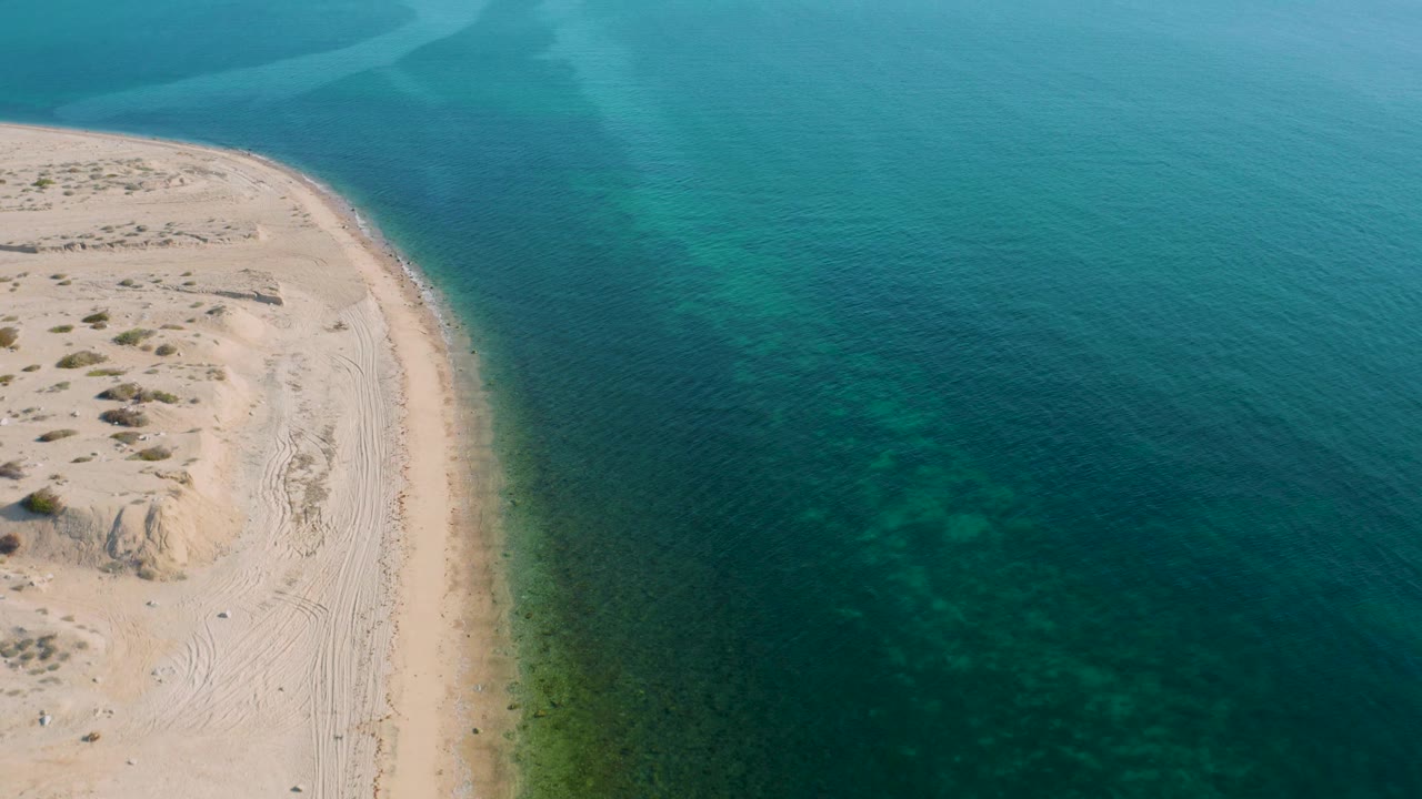 High drone view of El Sargento La Ventana, Mexico, with the sandy point compressed along the left edge and broad aquamarine water spreading across the right, no visible people.