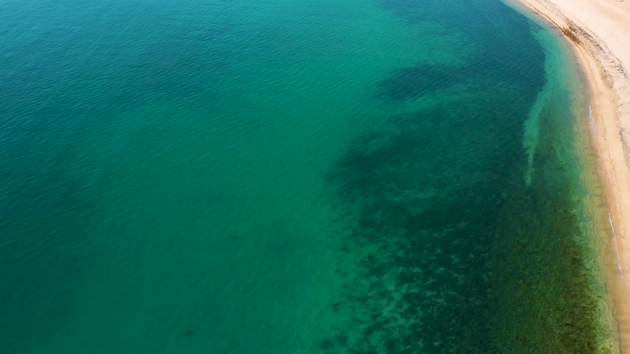 Green coastal water with dark sea bottom patches near the beach.