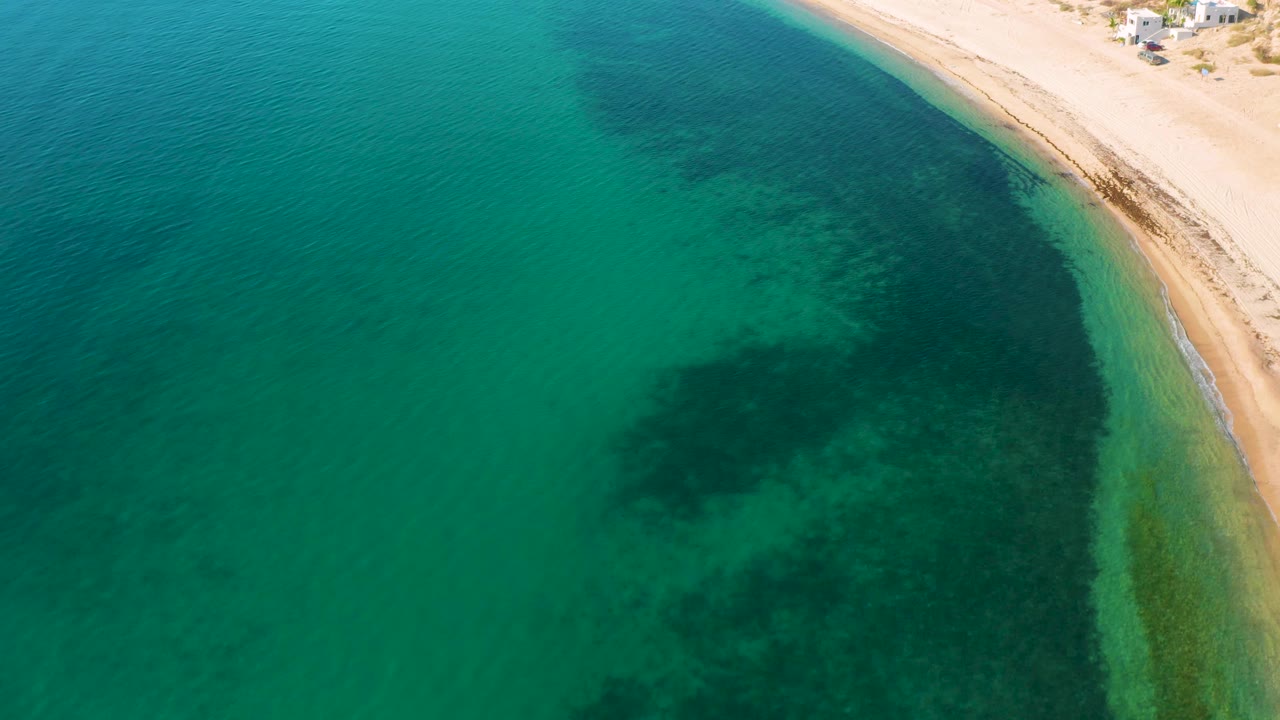 Aerial shoreline with green-blue water and dark seabed patches