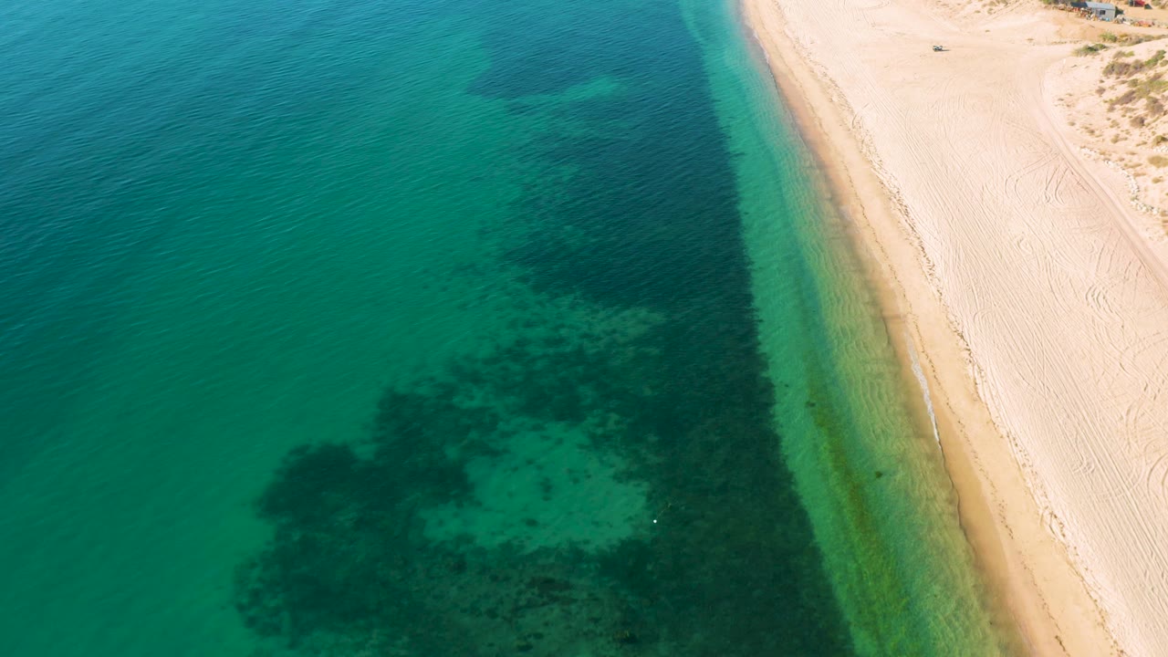 High drone-style view in El Sargento La Ventana, Mexico, with turquoise sea, a thin tan shoreline, open pale beach, and no visible people.