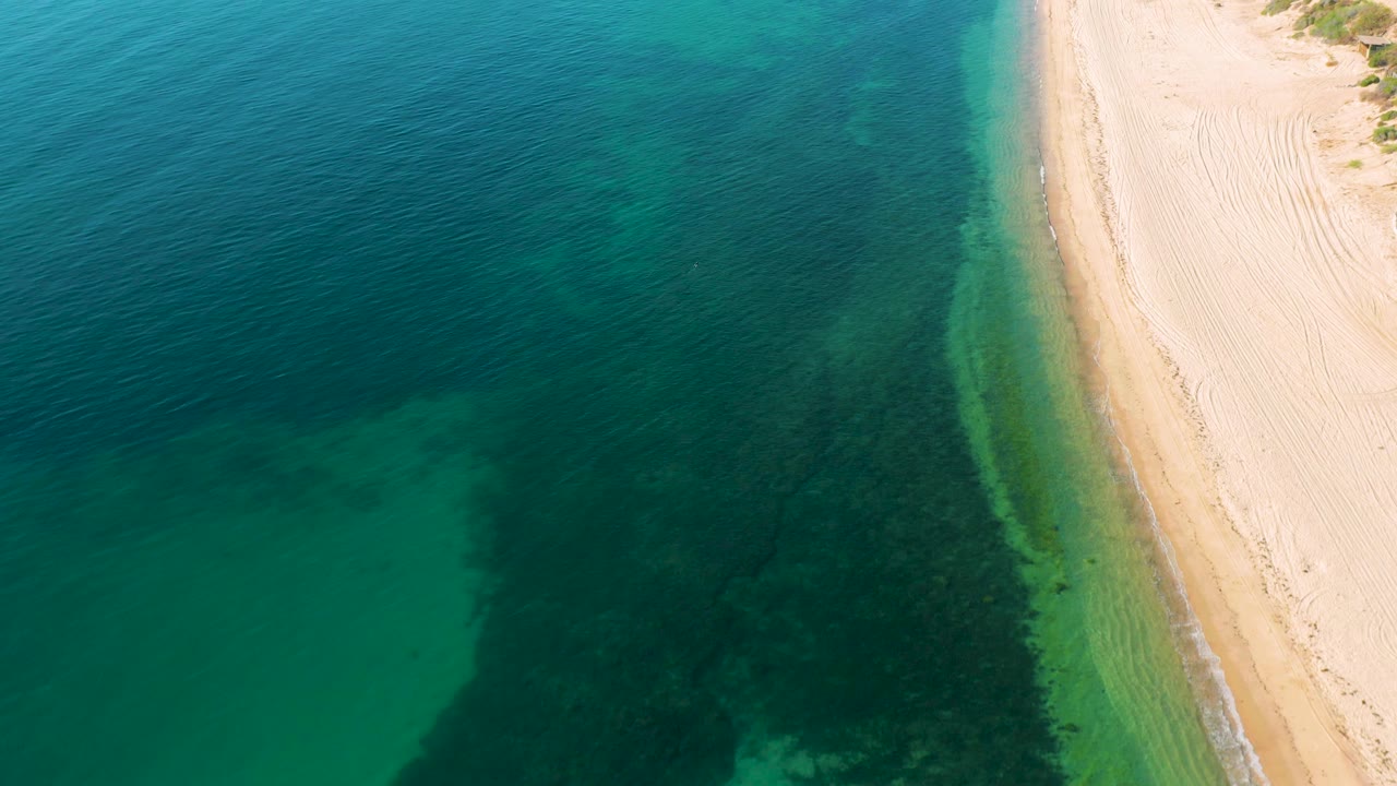 Drone view of green water meeting pale beach sand