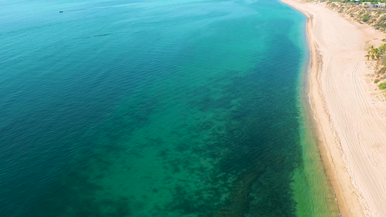 Top view of deep blue water and a thin sandy beach.