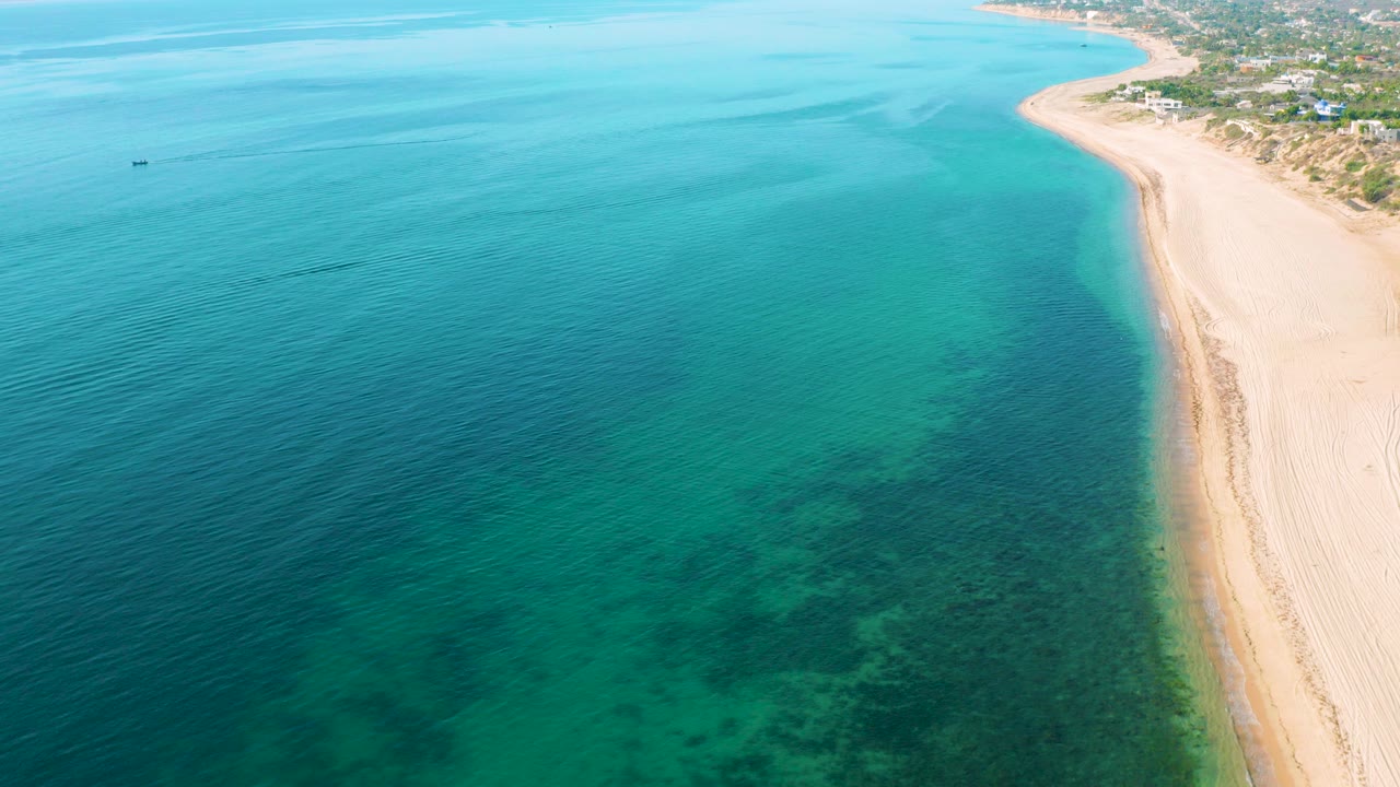 Aerial view of turquoise water beside a pale sandy beach.