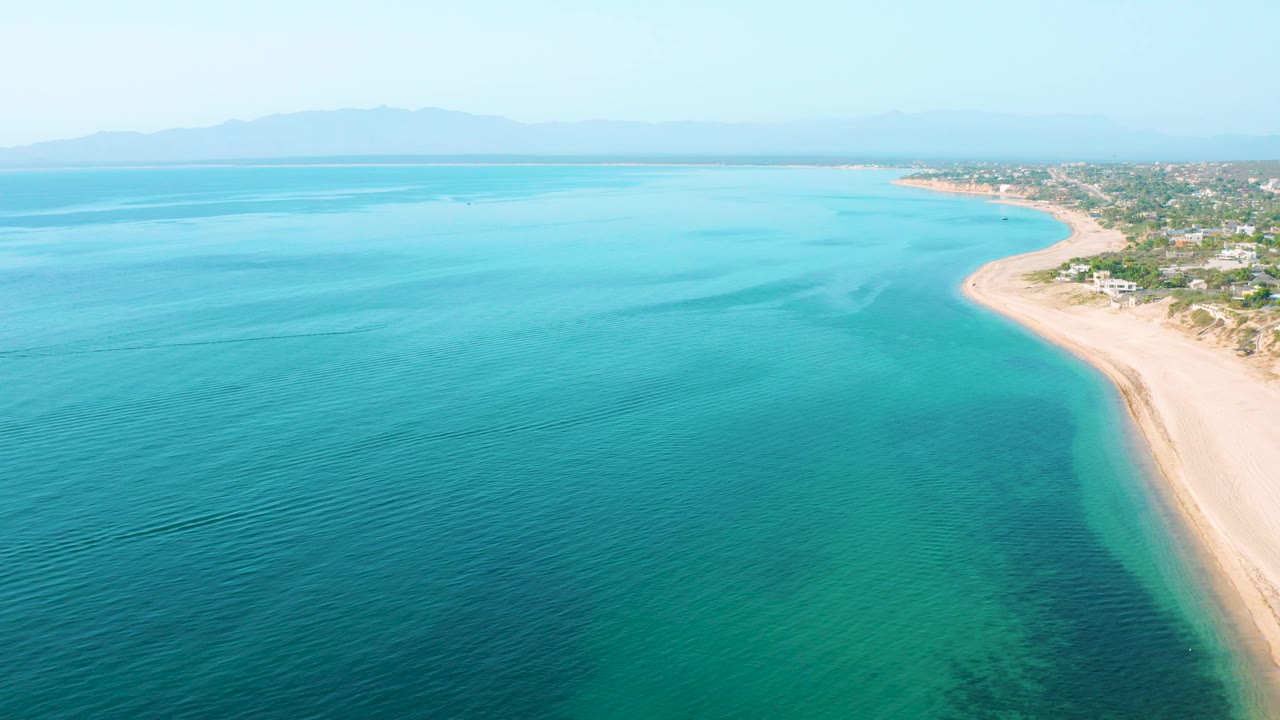 Aerial shoreline with turquoise water and beach homes in the distance.