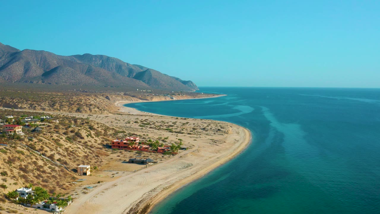 Third aerial frame over El Sargento La Ventana, Mexico, with ocean color bands to the right, sandy beach through the center, mountains to the left, and no visible people.