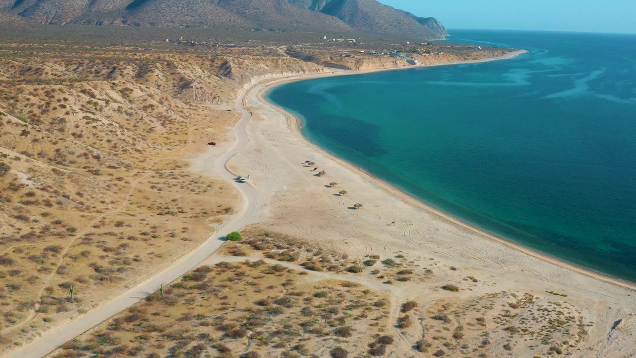 High coastal view with sandy shoreline, turquoise bay, and arid hills.