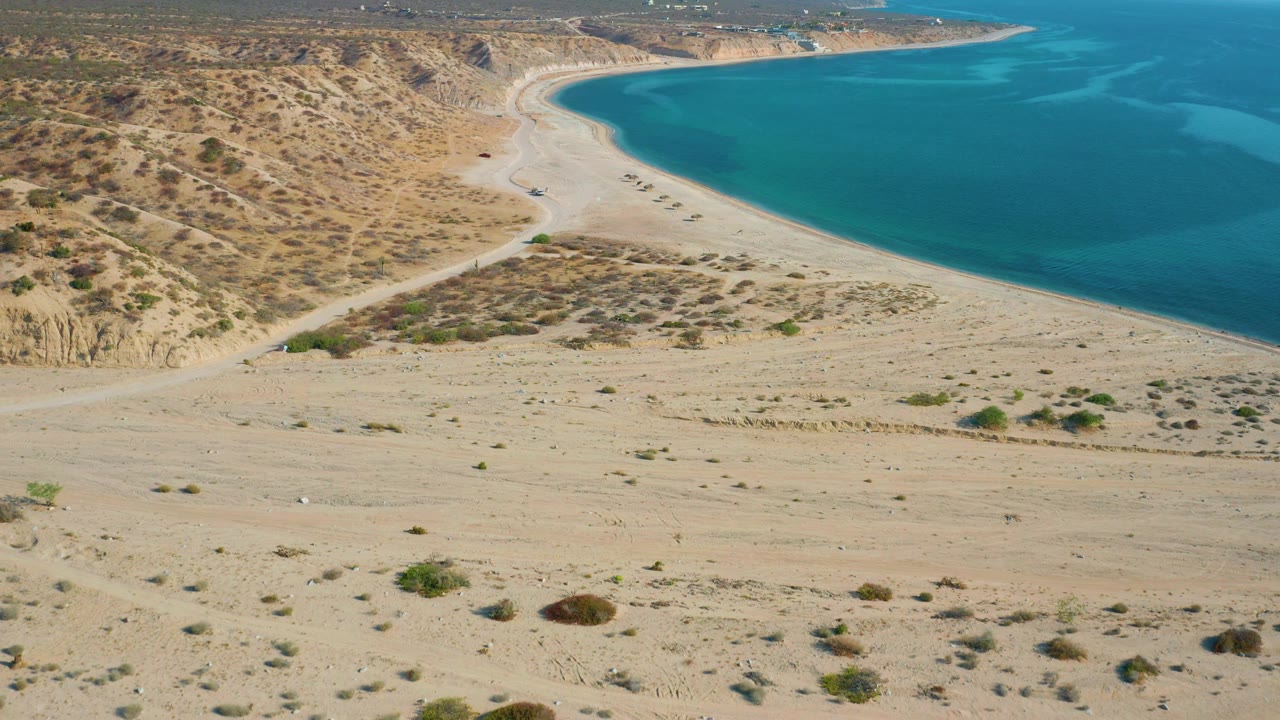 Aerial view over El Sargento La Ventana, Mexico, with sparse bushes dotting sand, eroded ground at left, the beach bend at top, and no visible people.