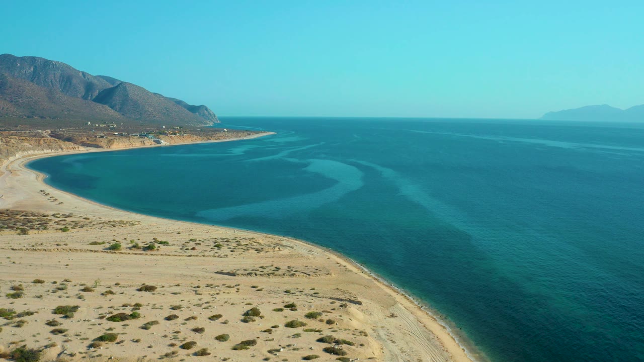 Aerial view of a quiet beach arc with turquoise water and mountains along the coast.