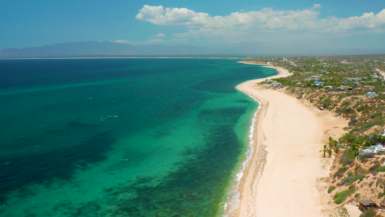 Aerial beach scene with shallow emerald water and a distant mountain horizon.