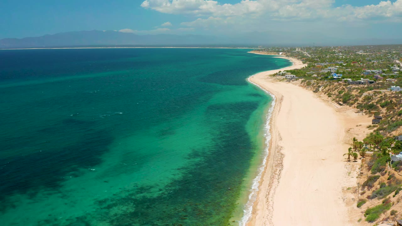 High coastal view with blue-green water, curving beach, and town edge.