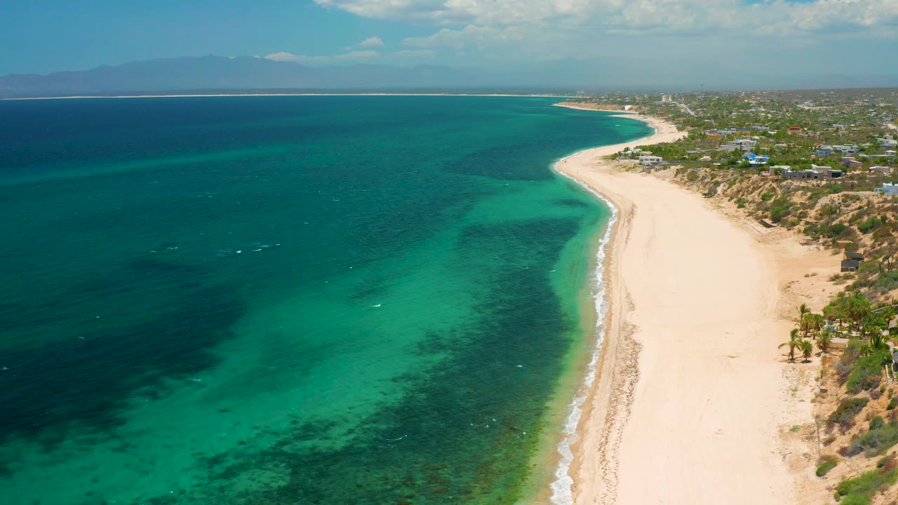 Wide aerial shoreline with teal water, empty beach, and coastal settlement.