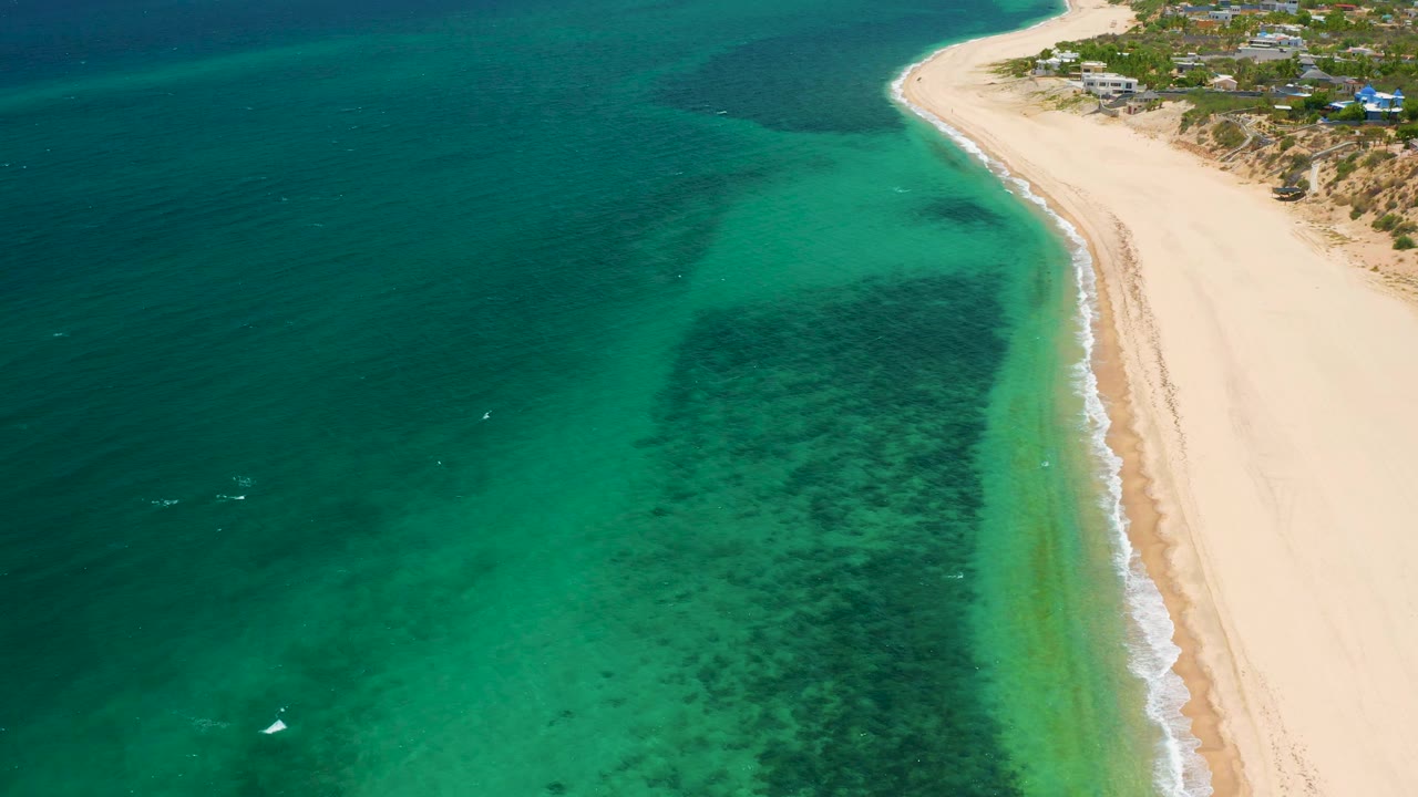 High aerial view in El Sargento La Ventana, Mexico, showing dark underwater reef or sea grass patches close to a pale beach and no visible people.