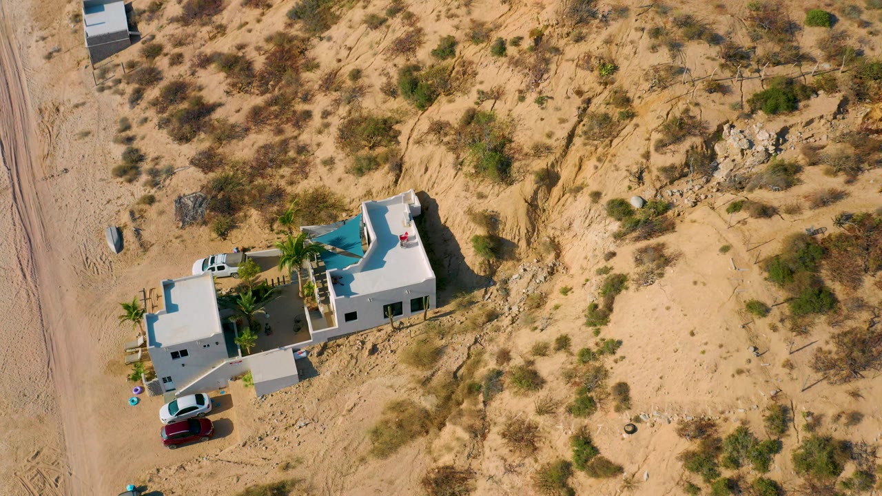 Aerial view of the villa beside a dirt road with scrub and rocks around it.
