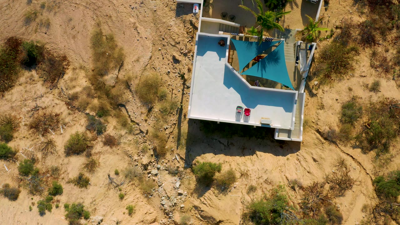 Third frame in El Sargento La Ventana, Mexico, keeps the white residence near the upper left, with dry tan earth, scrub, rocks, and no visible people around it.