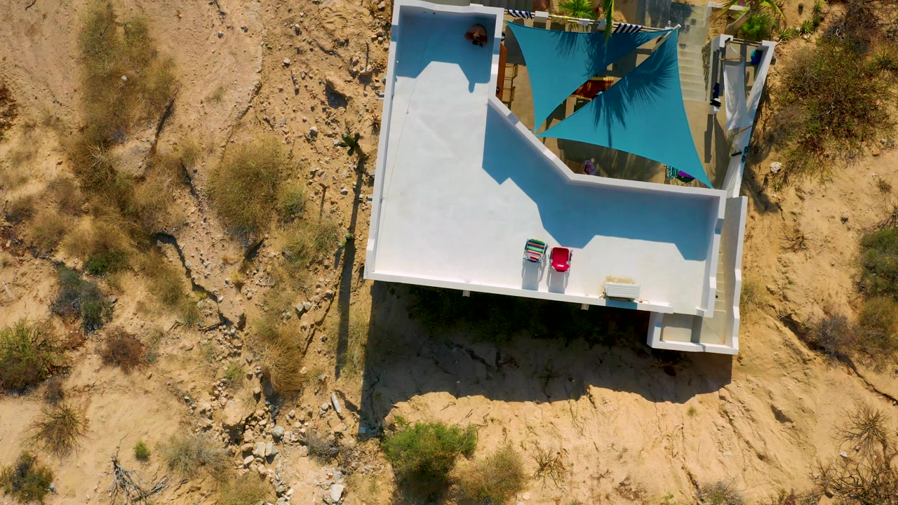 Aerial frame in El Sargento La Ventana, Mexico with the white roof and terrace on the left, scrubby sandy land on the right, a turquoise canopy, and no visible people.