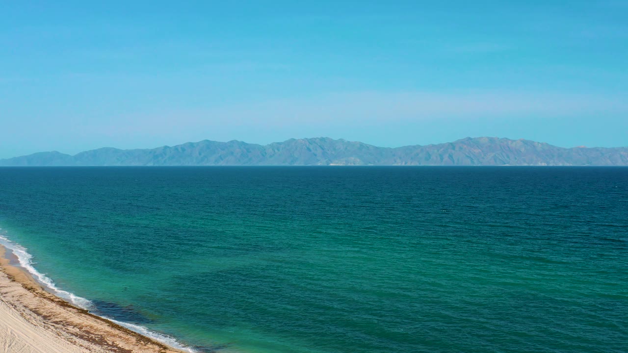Wide water surface with shoreline corner, mountains, and blue sky.