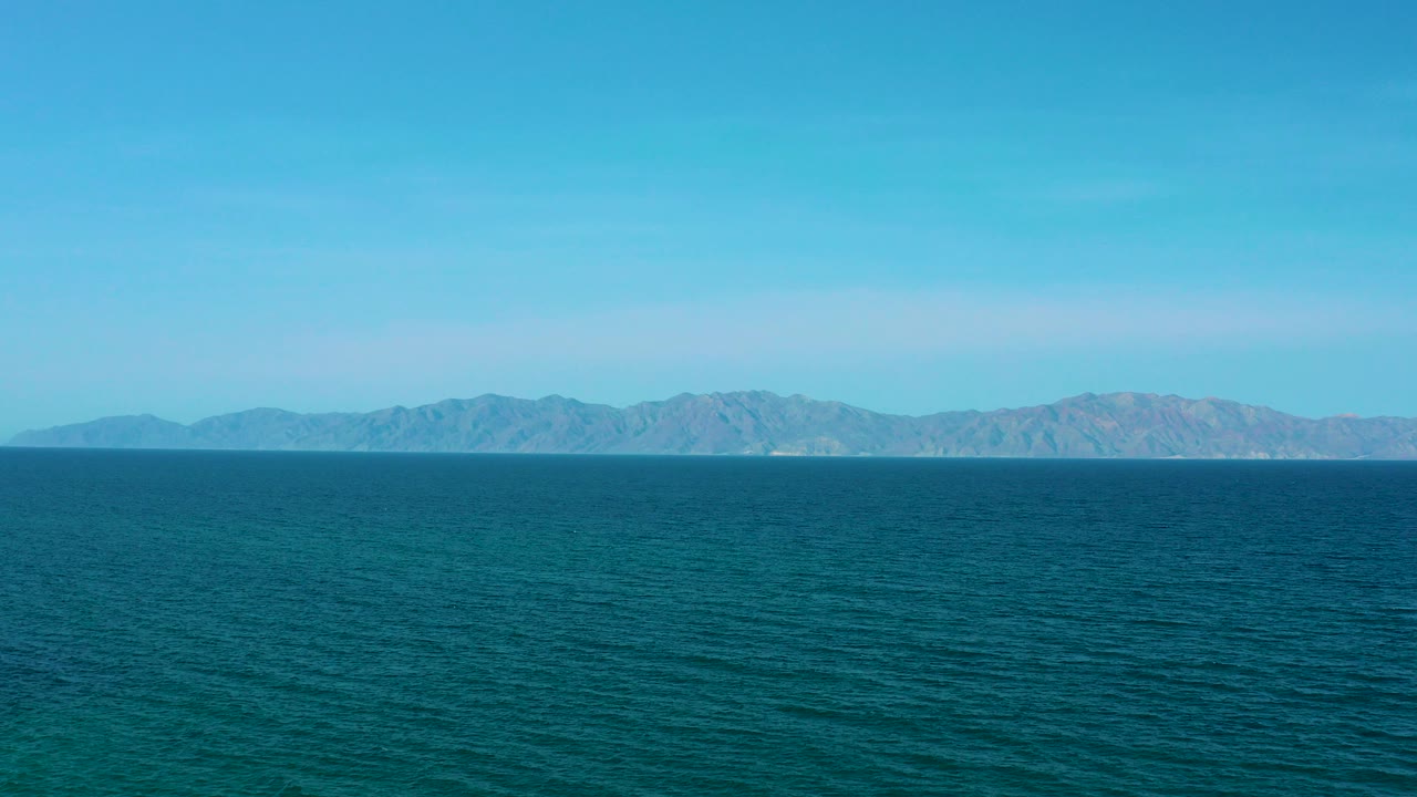 Wide blue sea with distant low mountains under clear sky