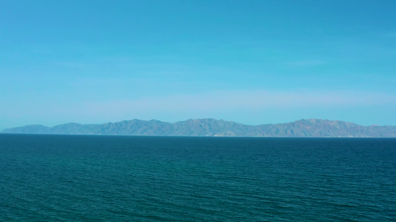 Mid-clip frame with blue sea filling the lower half, distant mountainous shoreline running across the background, clear sky above, and no visible people.