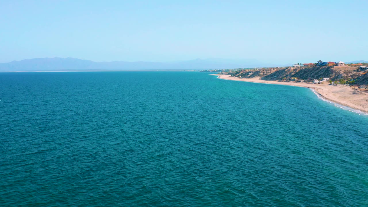 Ocean foreground leading to a tan beach and distant coastal land.