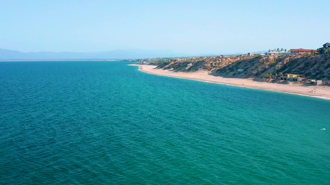 At two seconds, broad turquoise water dominates the foreground while the El Sargento La Ventana beach and bluff line stay high in frame, with no visible people on the sand.