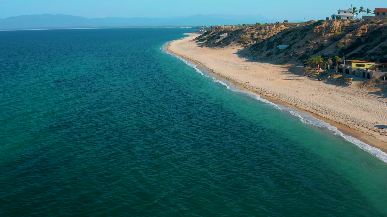 Blue ocean and sandy beach beneath sunlit coastal bluffs.