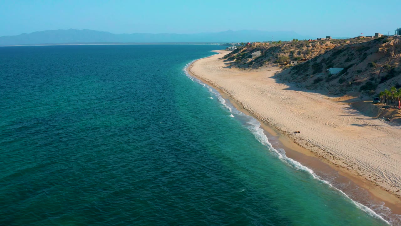 The second frame holds a diagonal drone view over turquoise shallows, white surf lines, a broad empty beach, scrub-covered dunes, and no visible people in El Sargento La Ventana, Mexico.