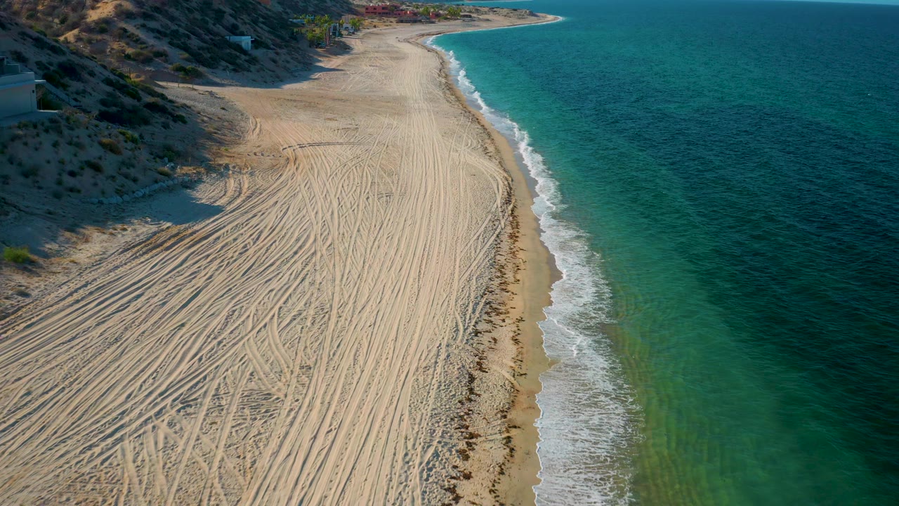 High shoreline view with tire tracks, surf, and hillside coast