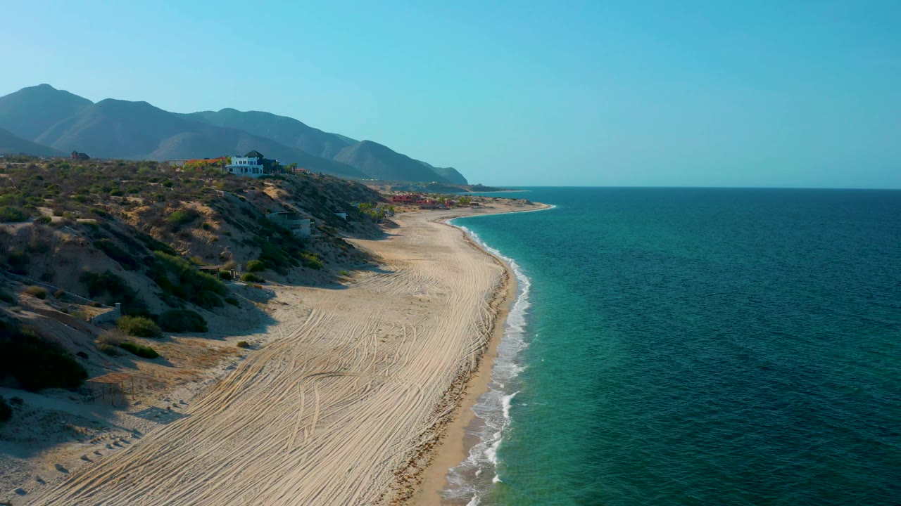 Empty beach with rolling surf beneath scrub-covered hills.