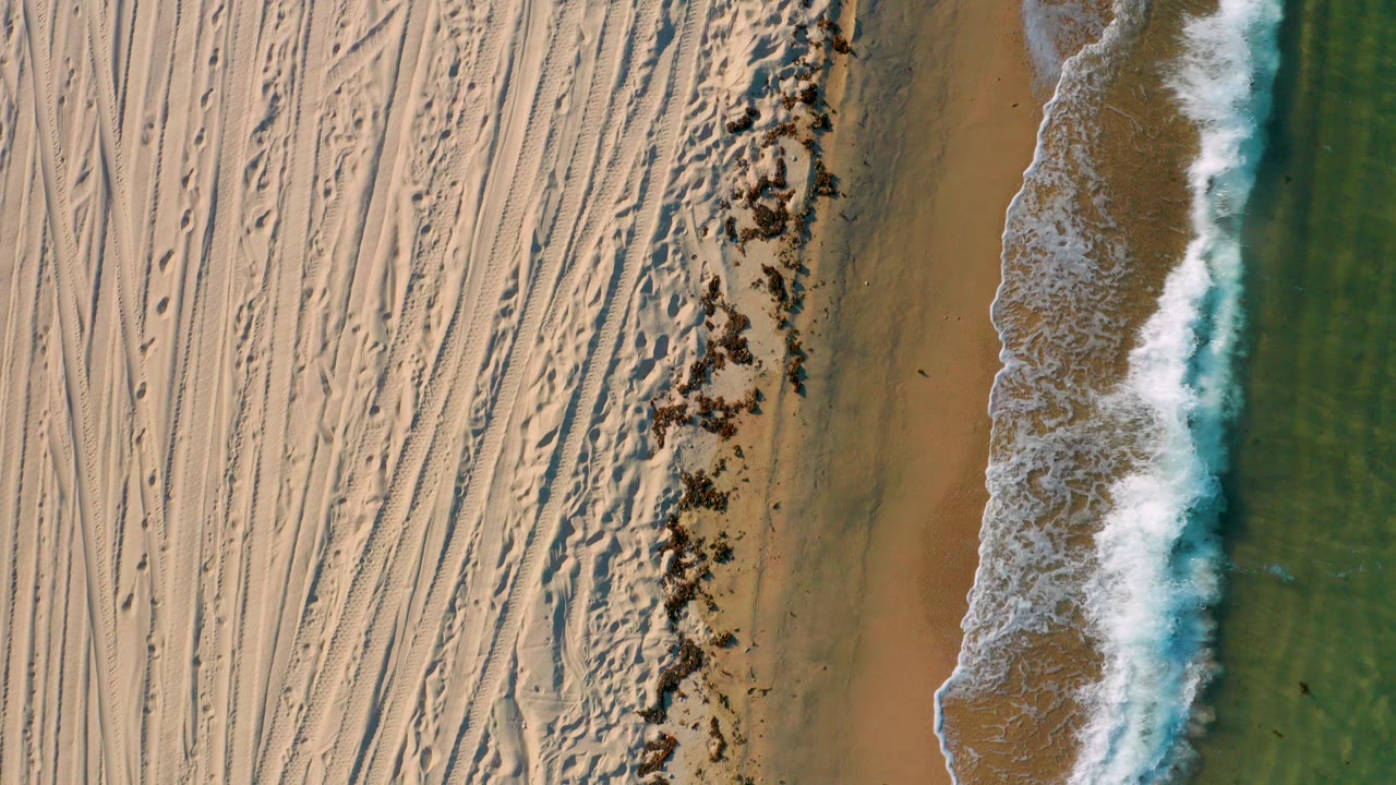 Overhead surf beside tracked sand and green water.