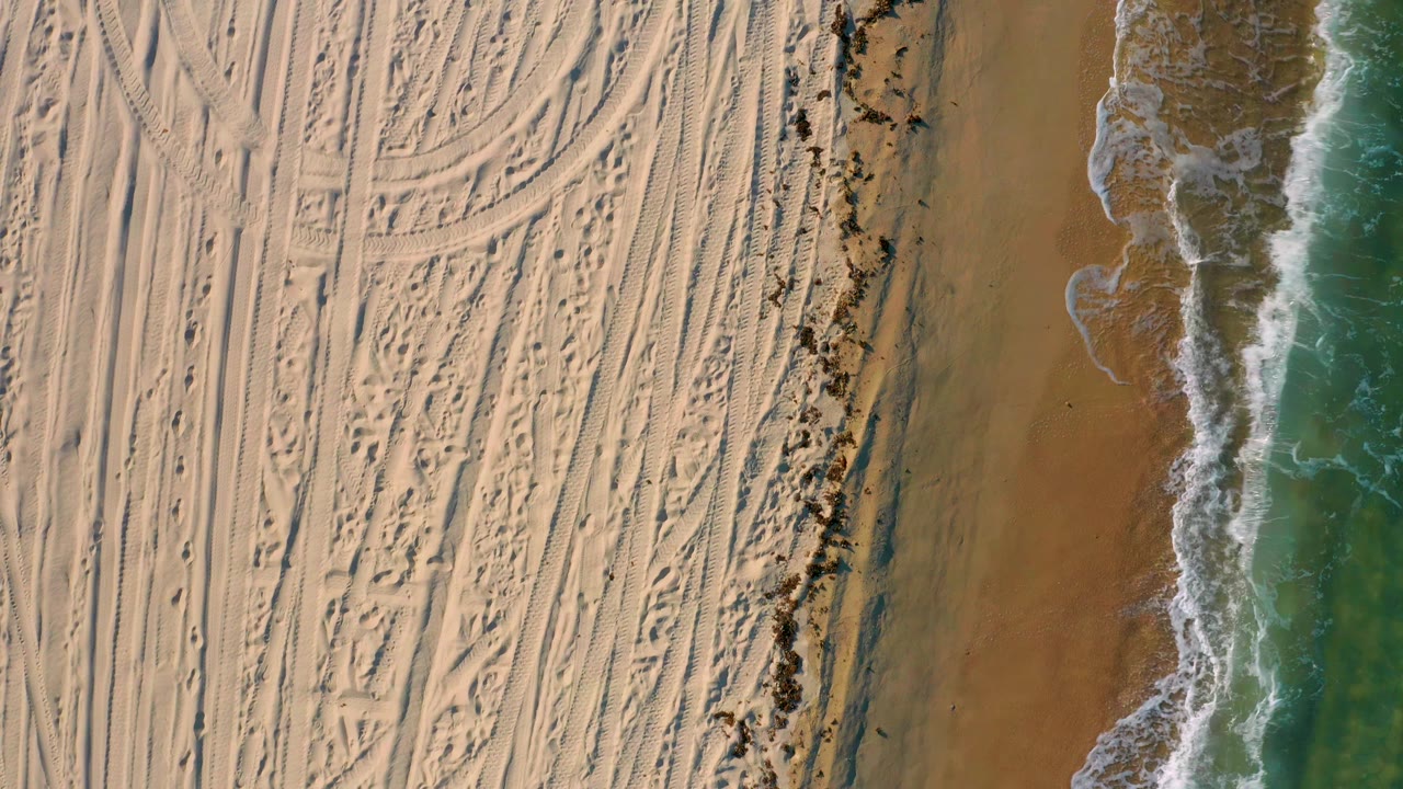 Patterned beach sand beside a foamy wave line.