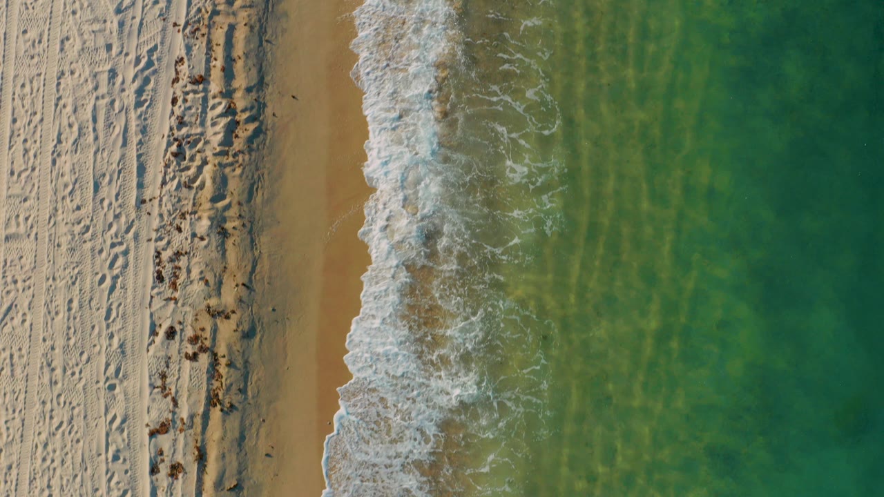 Overhead beach with sand, foam, and green-blue water