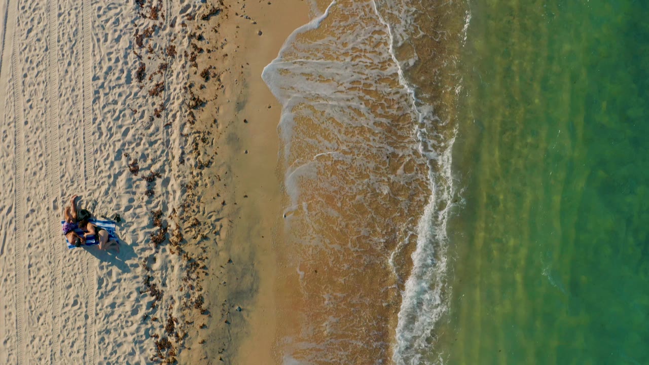 Overhead surf washing onto sand beside green ocean and marked beach.