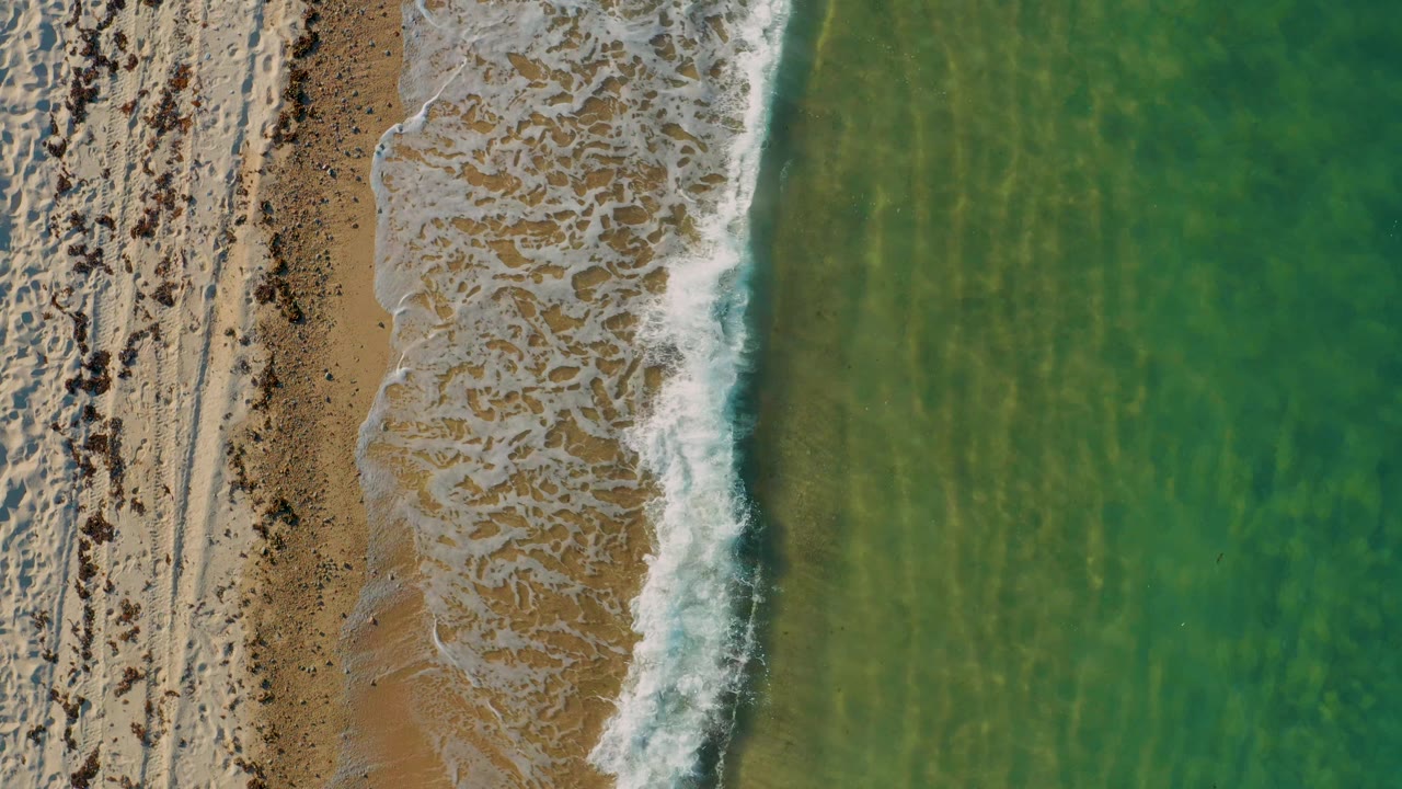 Surf curling over sand with green water beside it
