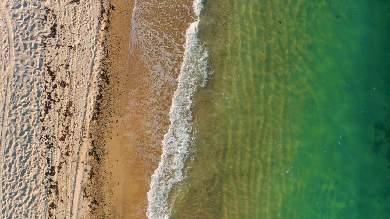 Overhead frame from El Sargento La Ventana, Mexico, showing pale sand on the left, a thin breaking wave near center, green water on the right, and no visible people.