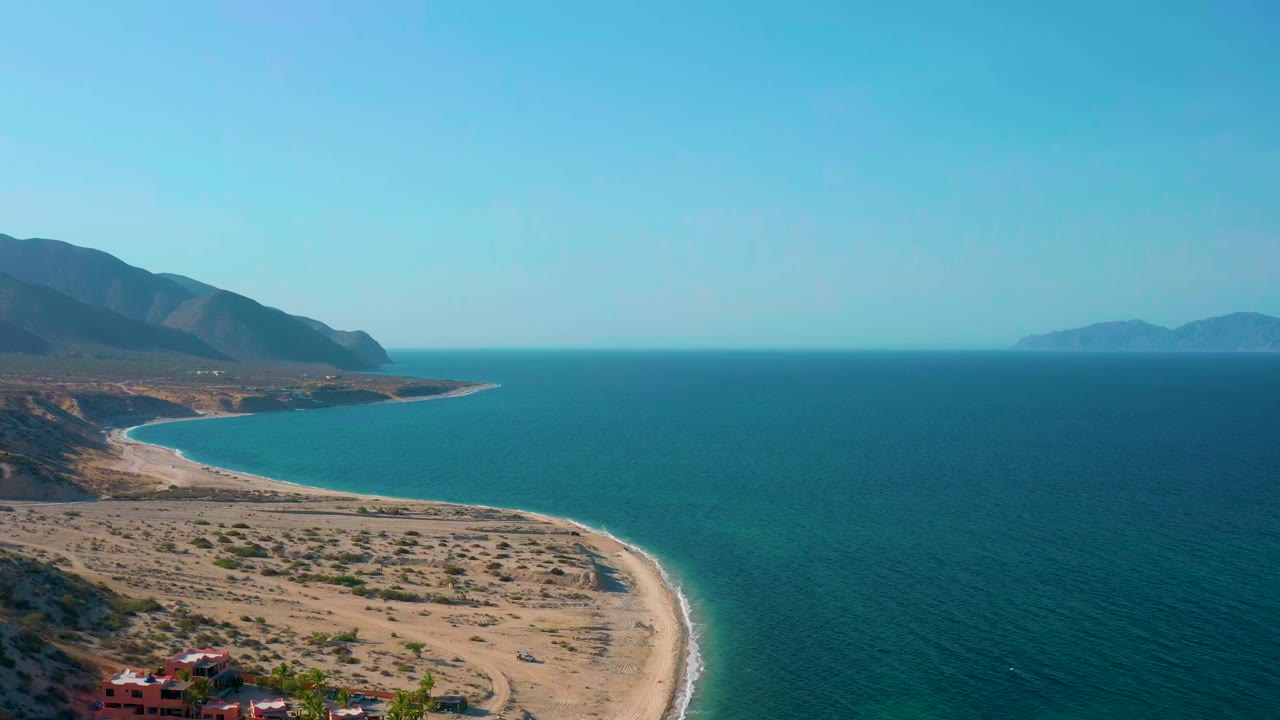 High coastal view with sandy beach, open sea, mountains, and distant islands.