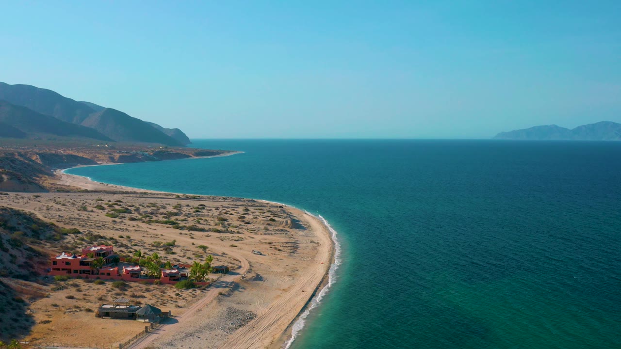 High coastal view with beach in foreground, village at bottom left, and mountains in back.