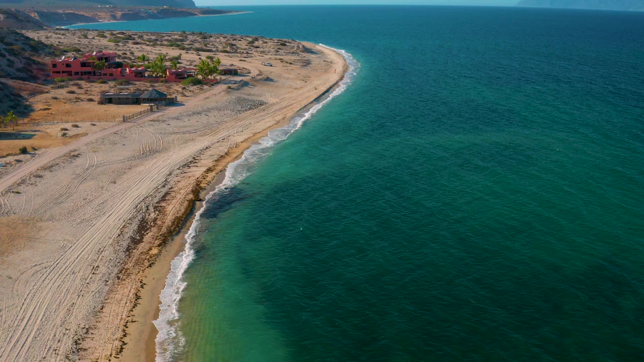 Curving shoreline with tire-marked sand and green-blue water.