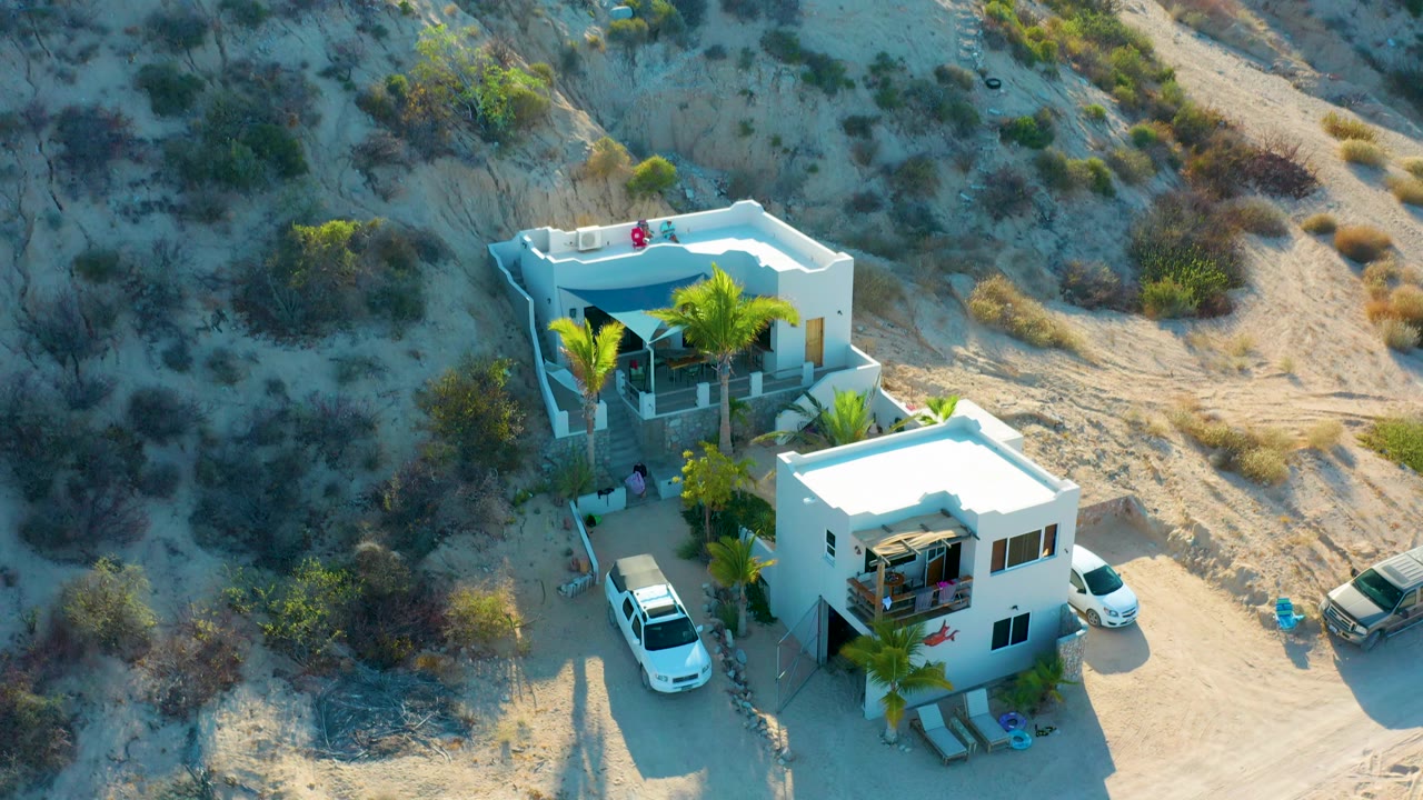 Aerial view of two white houses at the base of a scrubby desert slope.