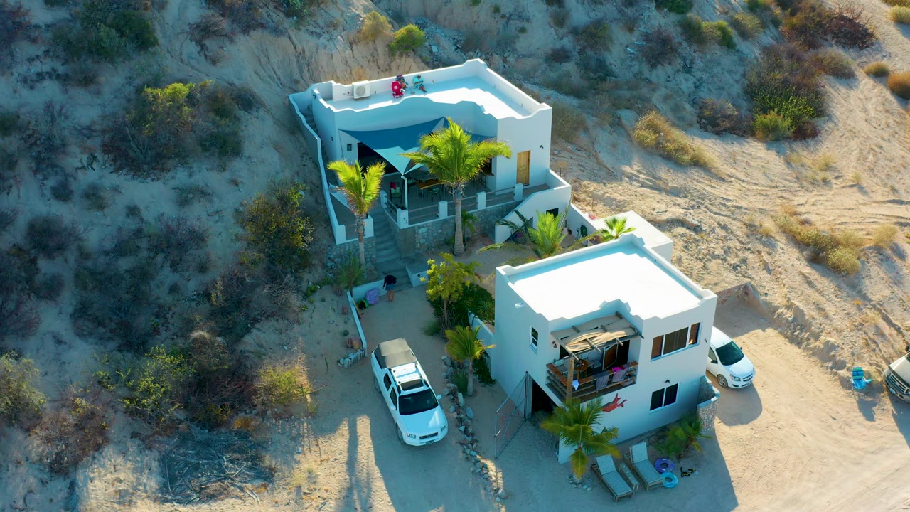 The overhead view in El Sargento La Ventana, Mexico shows the two white buildings separated by sandy paths, with palms casting shadows and small figures visible on the property.
