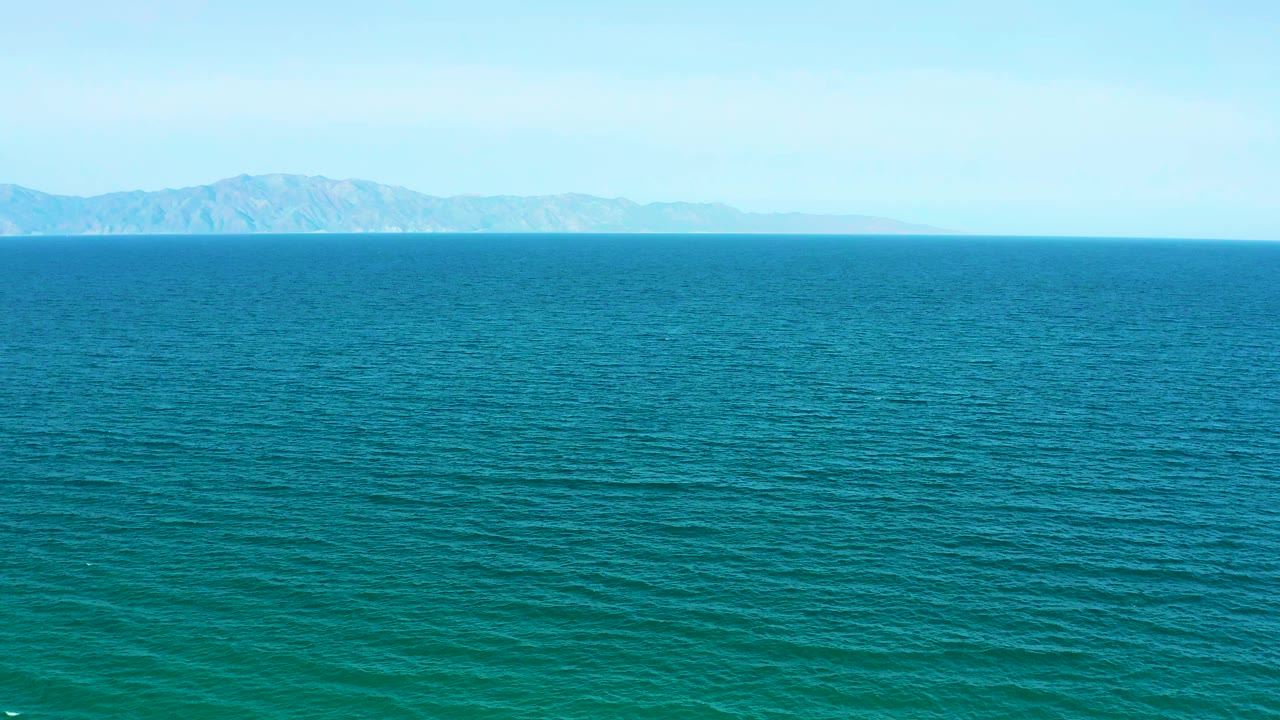 Opening frame of rippling blue water near El Sargento La Ventana, Mexico, with hazy mountains on the horizon and no visible people.