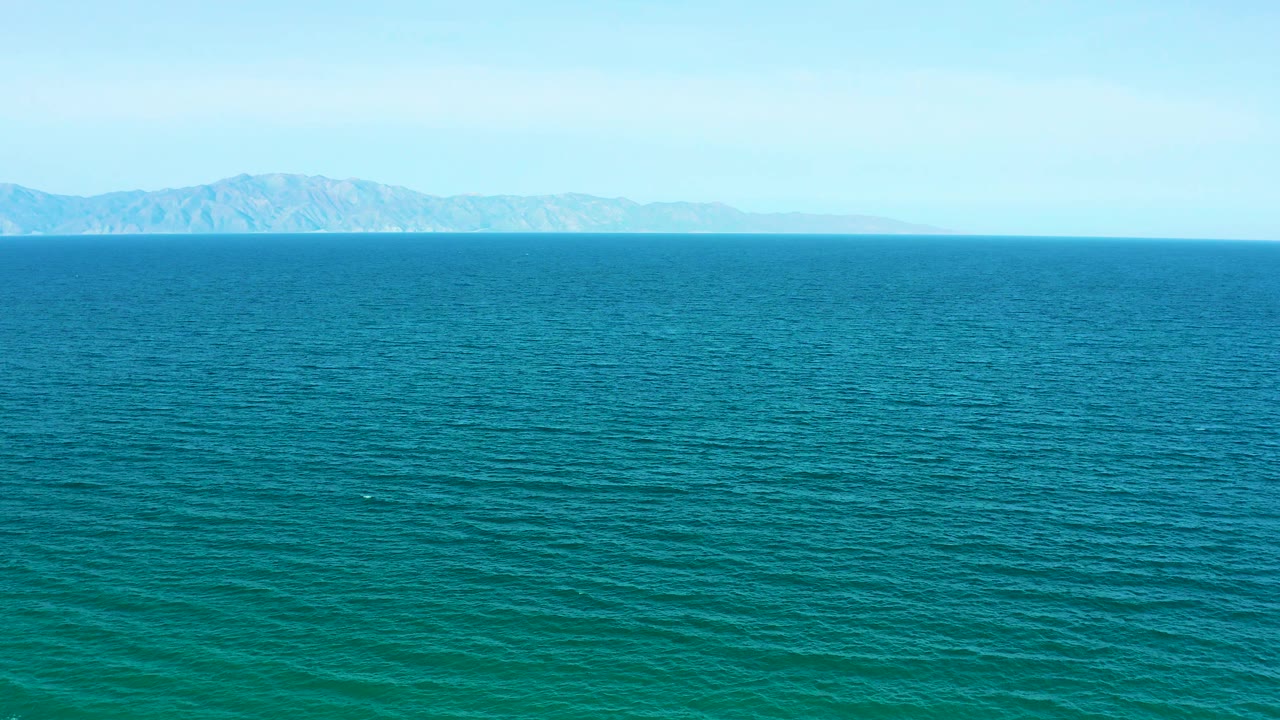 A broad field of blue water stretches toward low hazy mountains at El Sargento La Ventana, Mexico, with no visible people or boats.